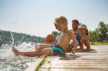 Family sitting together on a dock watching child splash in the water. 
