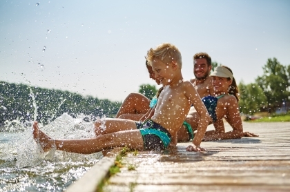 Family sitting together on a dock watching child splash in the water. 