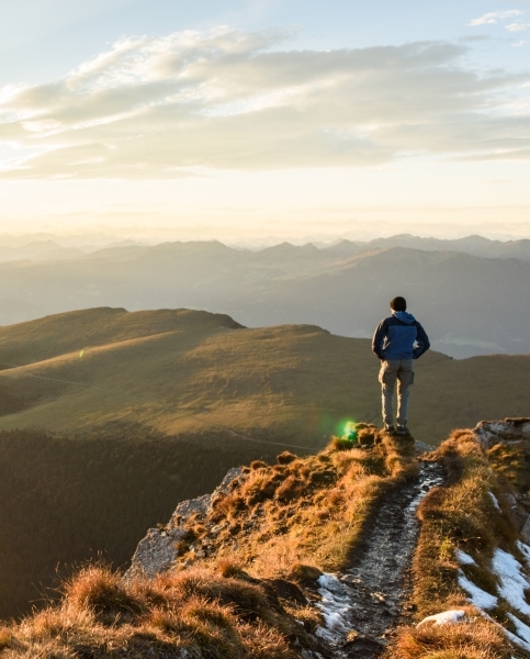 Full view of man at top of mountain looking down at sunset.