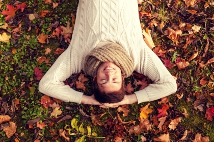 Man wearing a scarf and sweater laying on the grass covered in fall leaves.